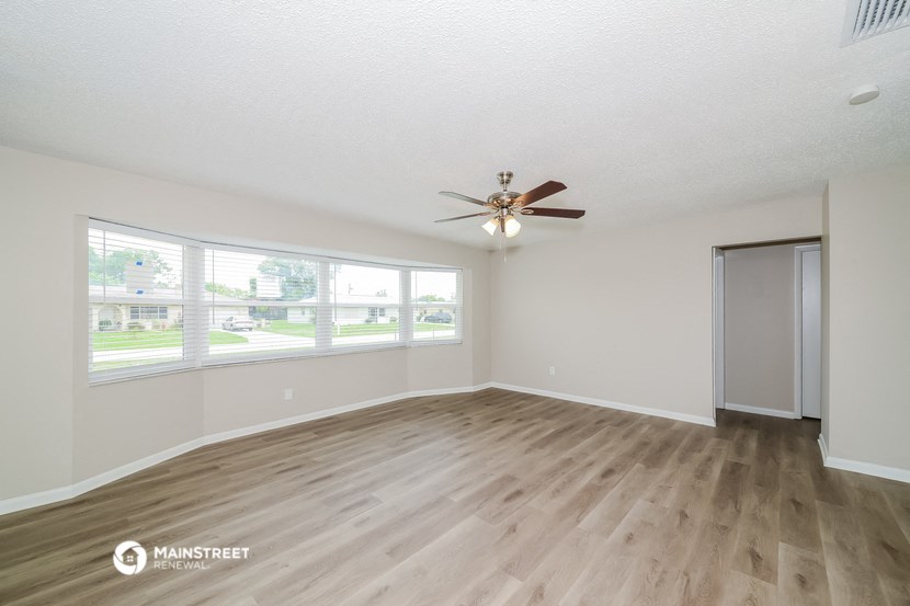 the spacious living room with wood flooring and a ceiling fan