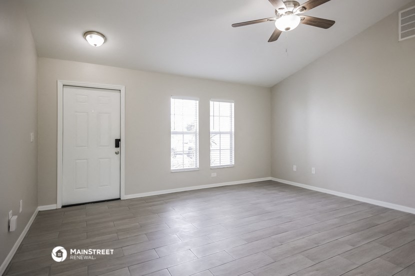 the spacious living room with white walls and a ceiling fan