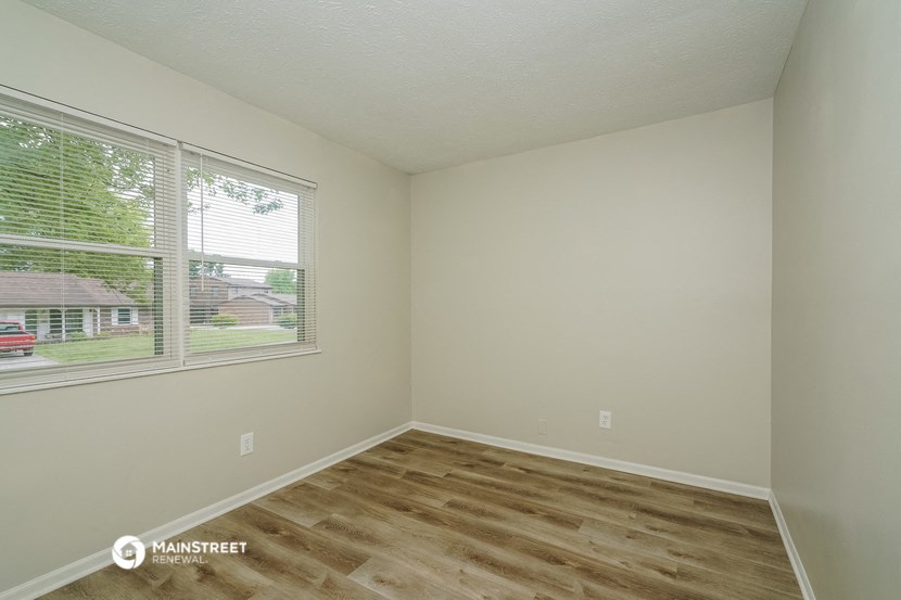 the spacious living room of an apartment with wood flooring and a large window