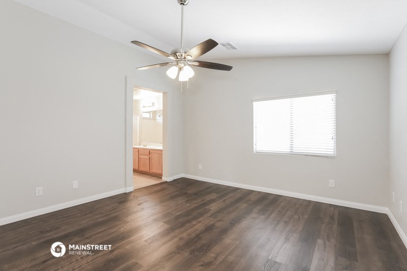 the spacious living room with hardwood flooring and a ceiling fan
