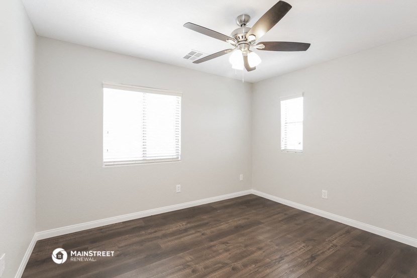 the spacious living room with wood floors and a ceiling fan