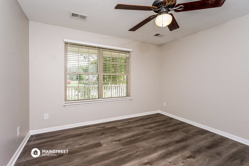 the spacious living room with a large window and a ceiling fan