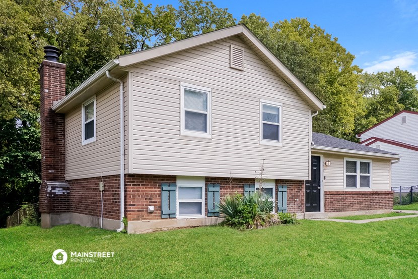 a white and brick house with a yard and trees in the background