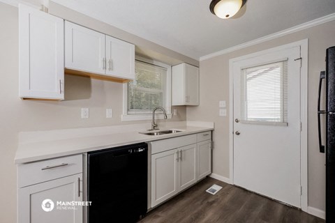 the kitchen of an apartment with white cabinets and a black dishwasher