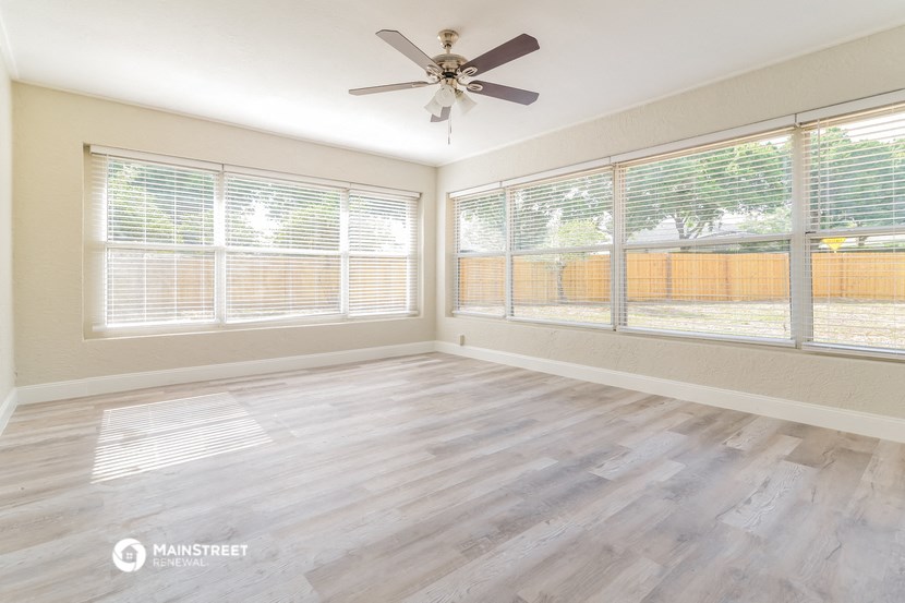 an empty living room with large windows and a ceiling fan