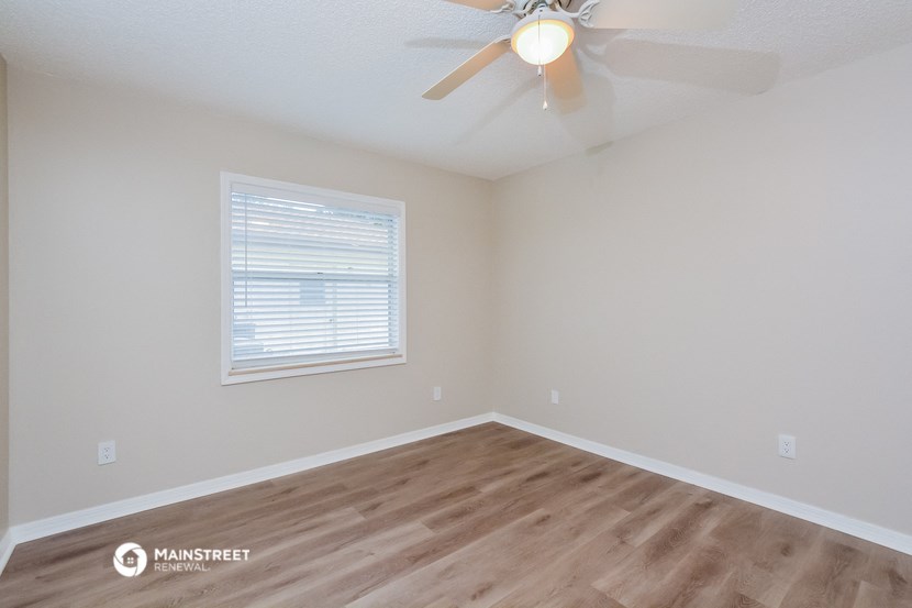 the spacious bedroom with hardwood flooring and a ceiling fan