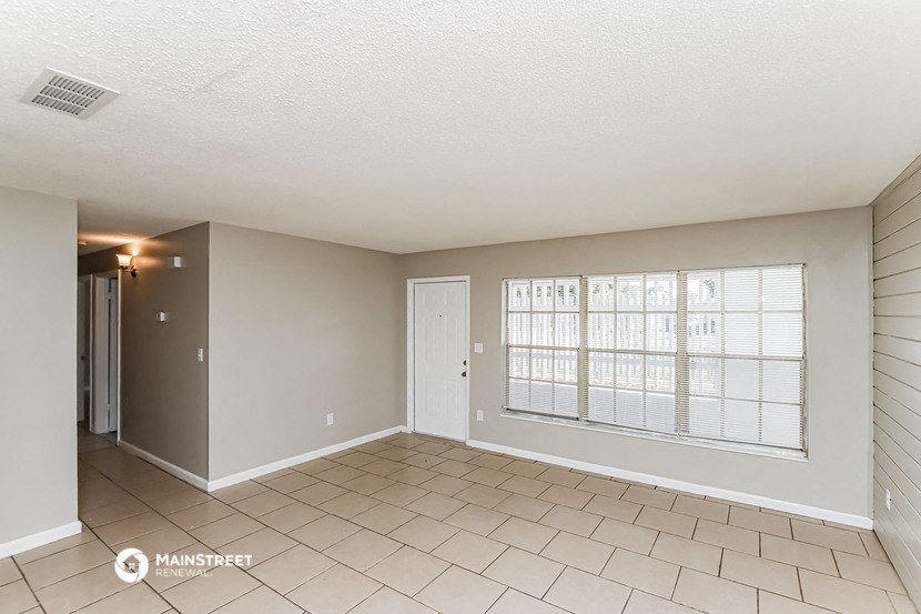 an empty living room with a large window and tiled flooring