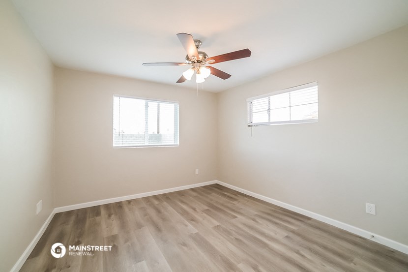 an empty room with a ceiling fan and two windows