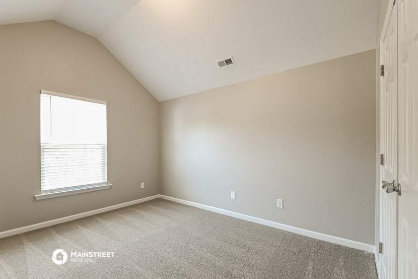 an empty bedroom with a window and carpeting