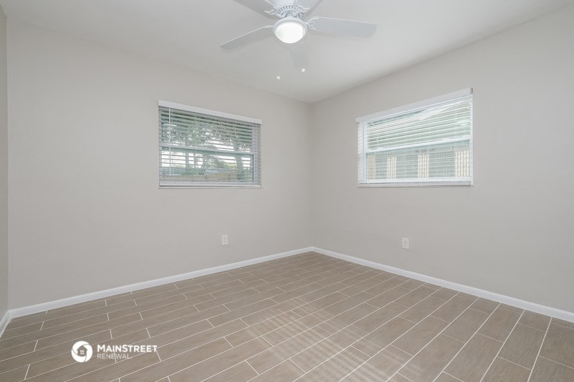 the spacious living room with two windows and a ceiling fan