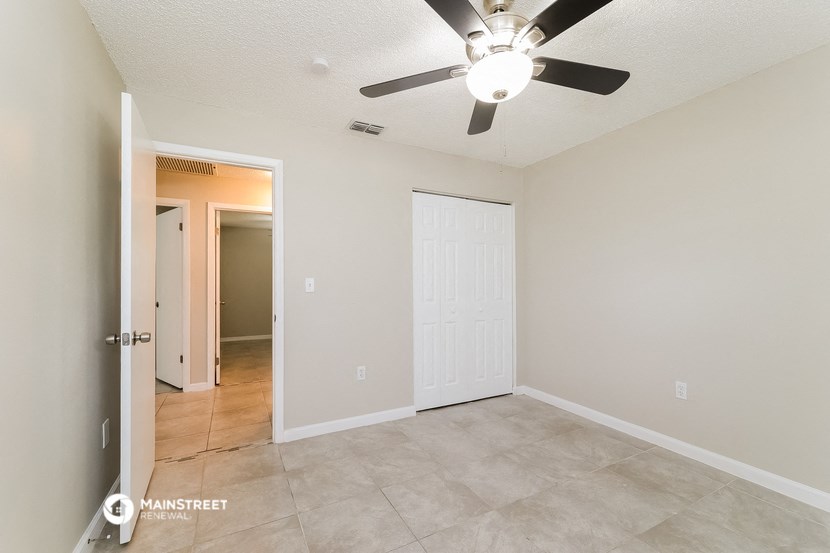 an empty living room with a ceiling fan and a door to a closet
