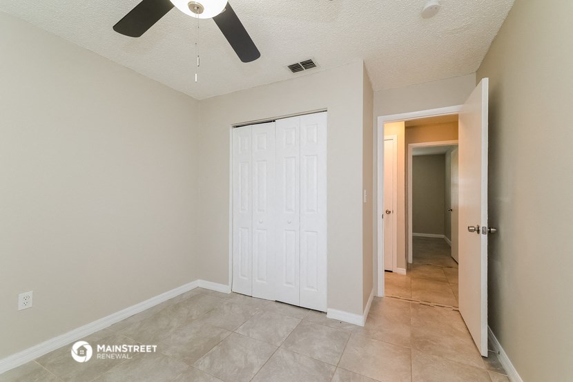 the living room of an empty home with a white door and a ceiling fan
