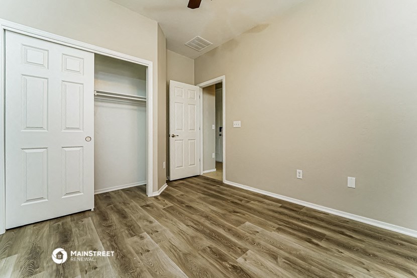 the living room and closet of an empty home with wood flooring
