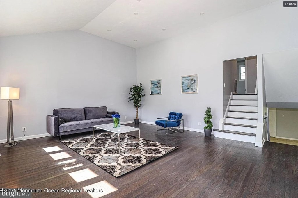 A living room with a grey couch, a blue chair, a coffee table, and a staircase.