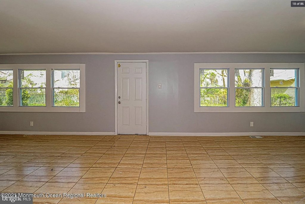 A room with a white door and windows with trees visible outside.
