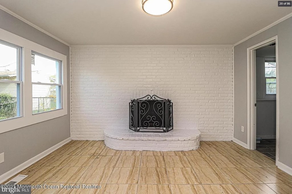 A white brick wall with a black fireplace in the middle of a room with wooden floors.