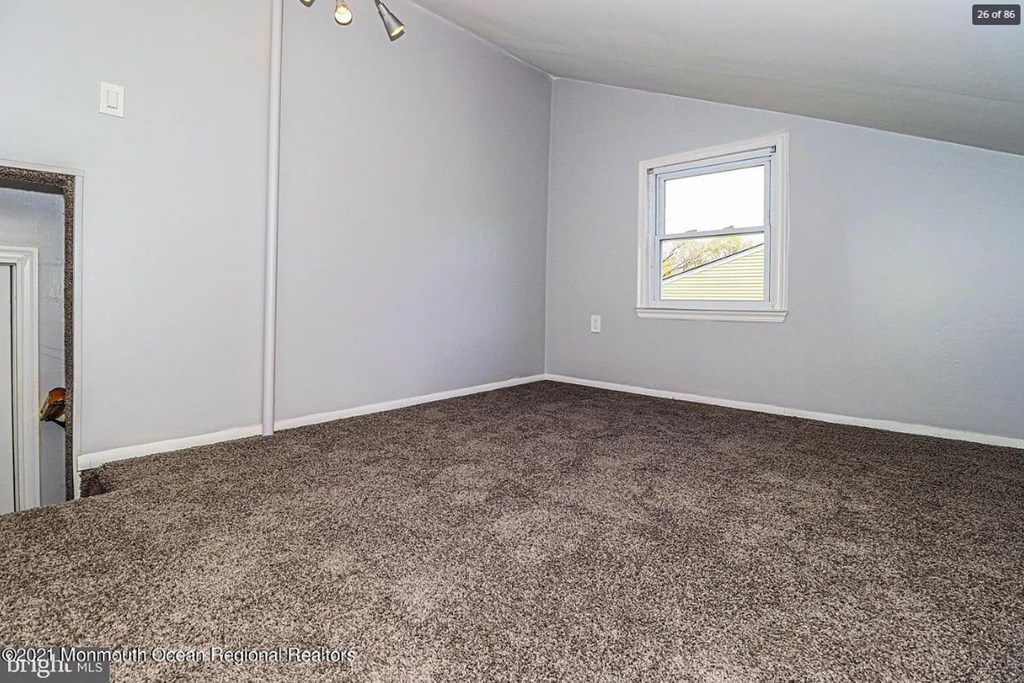 A room with a carpeted floor and a window showing a view of a road.
