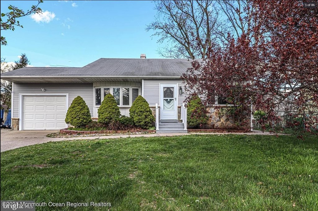 A house with a grey roof and a white garage door is surrounded by a green lawn.