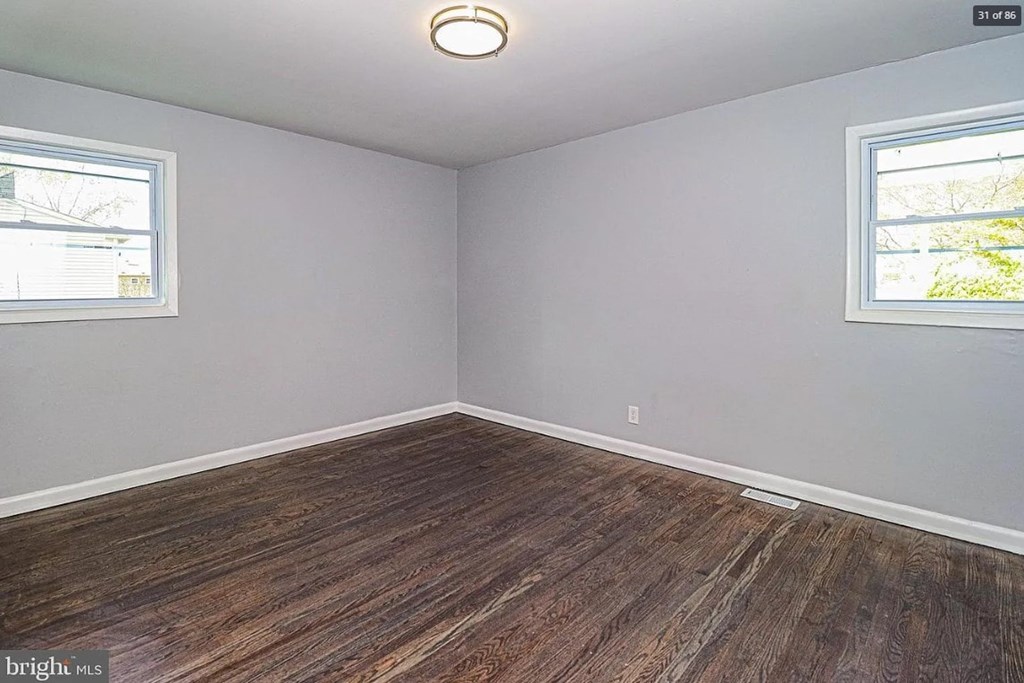 A room with wooden flooring and two windows.