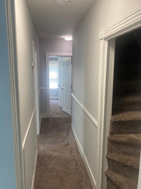 A hallway with a staircase on the right and a door at the end.