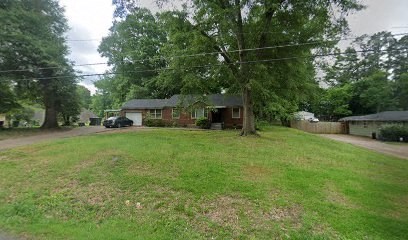 A tree in a yard with a house in the background.
