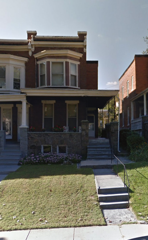 A brown house with a front yard and steps leading to the front door.