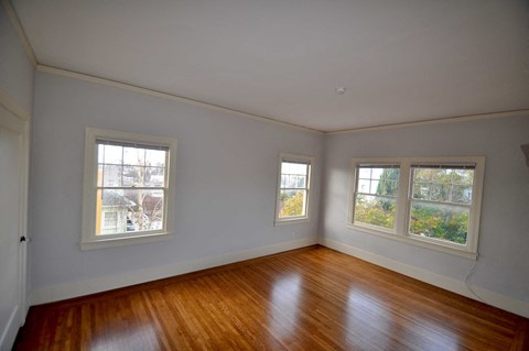 an empty room with wooden floors and three windows