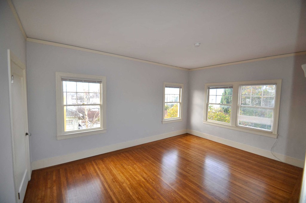 an empty living room with wood floors and three windows