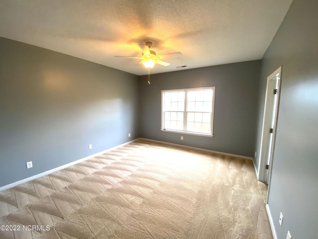 A room with a carpeted floor and a ceiling fan.