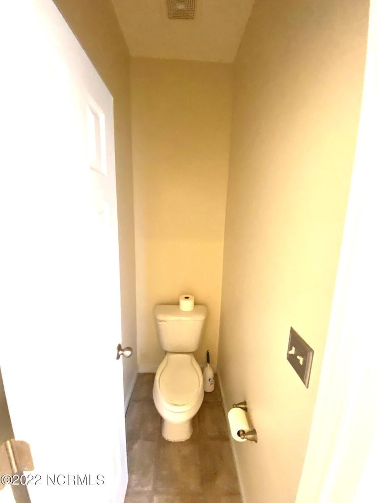 A white toilet is in a small bathroom with a door on the left.