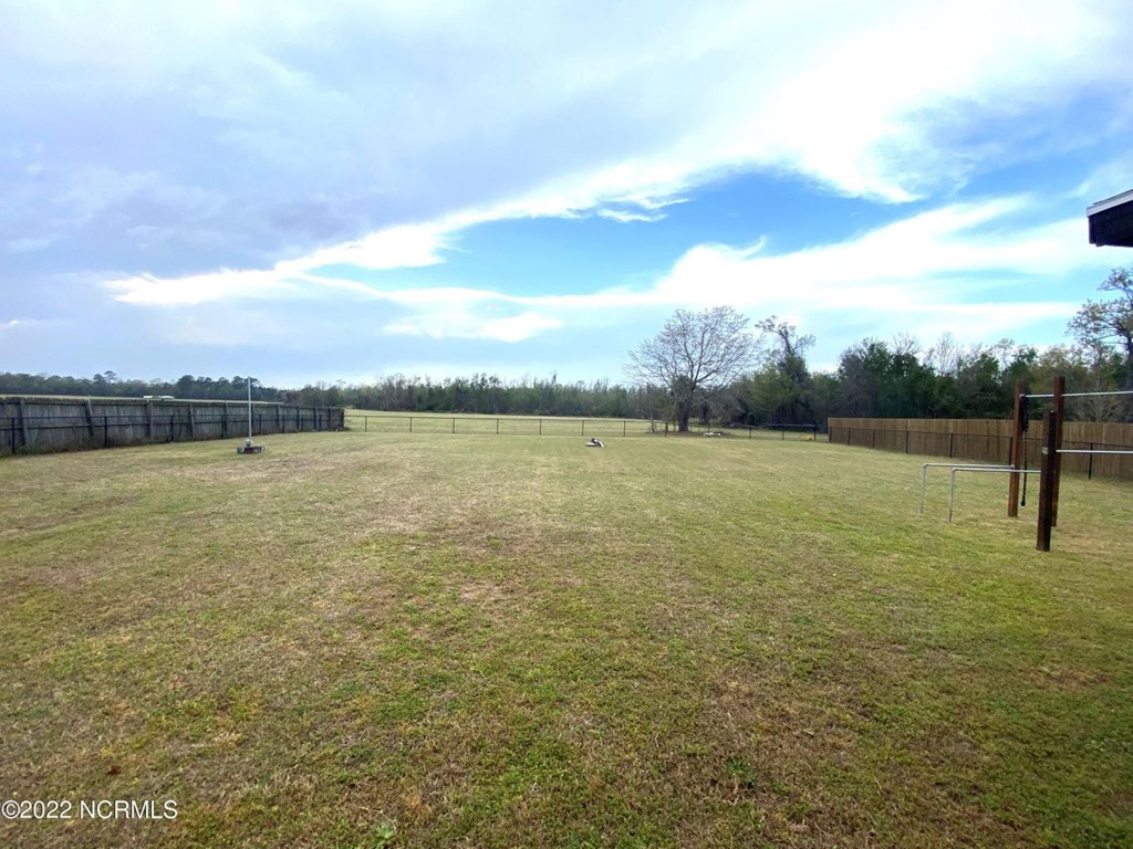 A large, open field with a fence and trees in the distance.