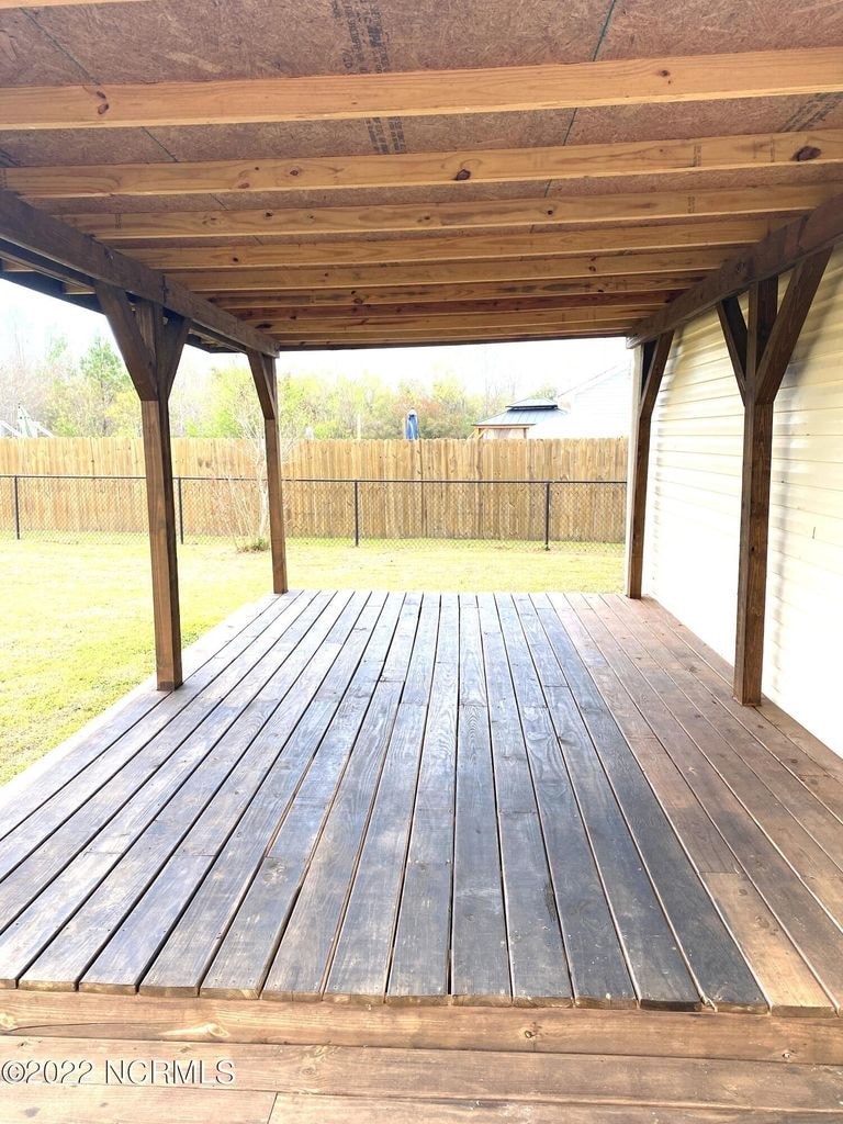A wooden deck with a roof and a fence in the background.