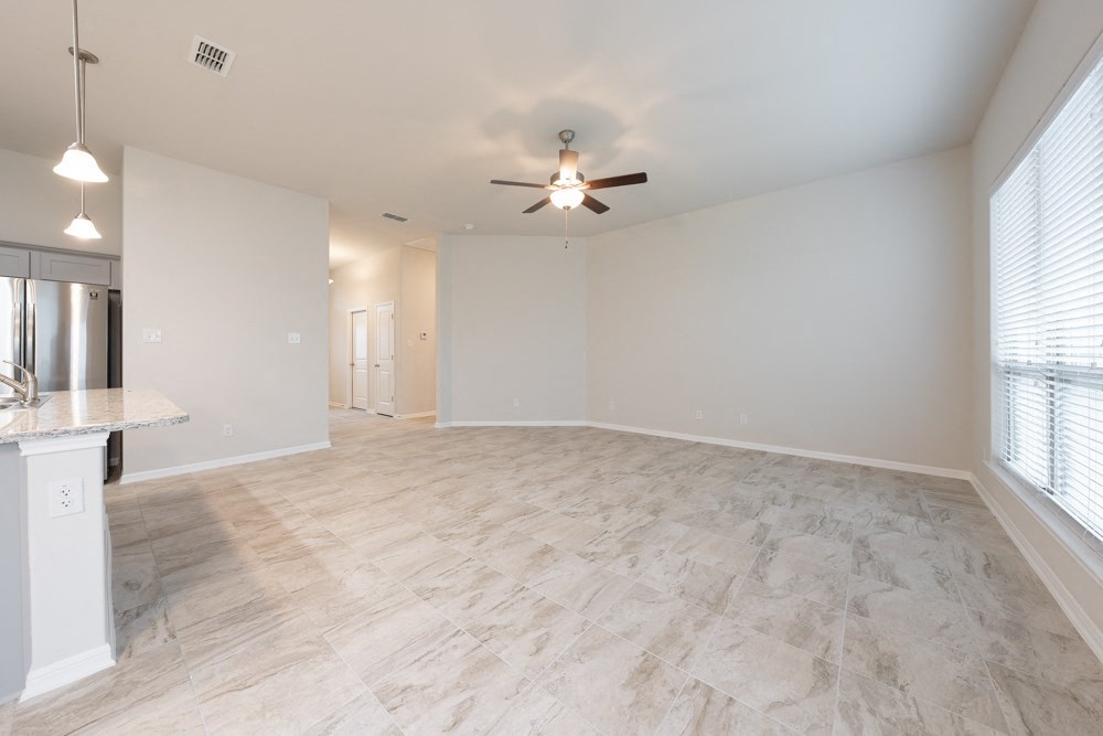 an empty living room with a ceiling fan and a kitchen