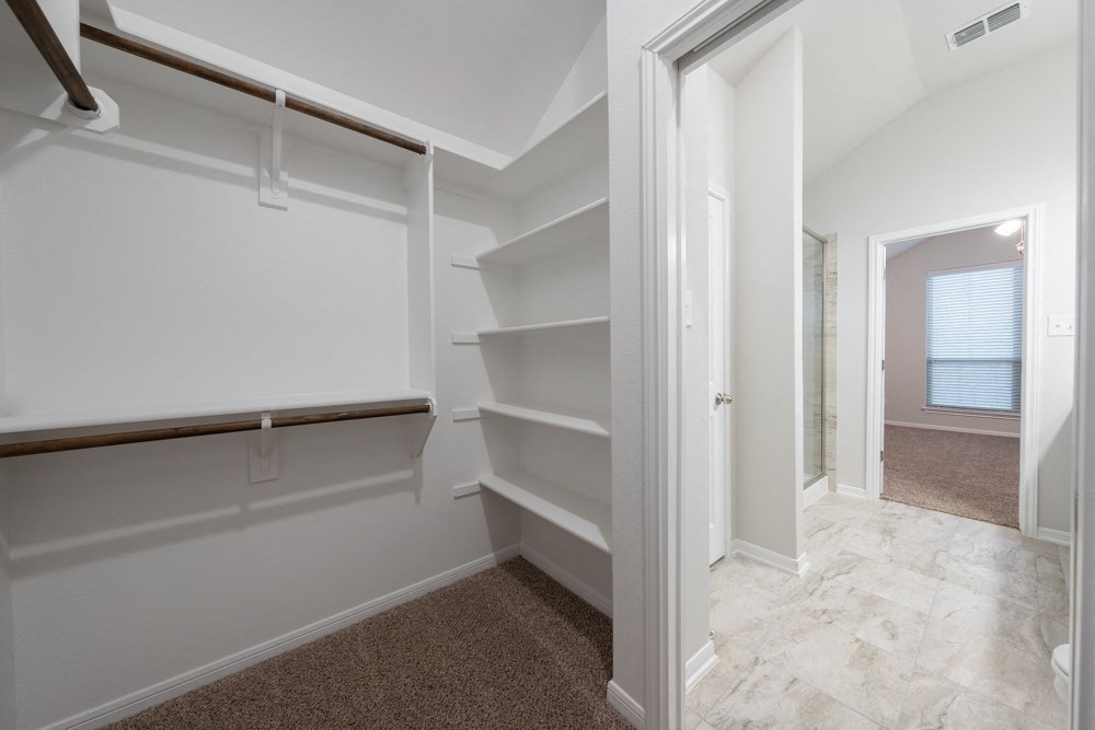 a walk in closet in a home with white walls and shelves