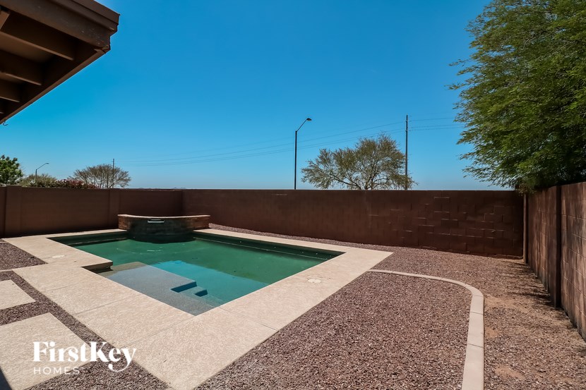 A pool surrounded by a brown fence and a stone patio.