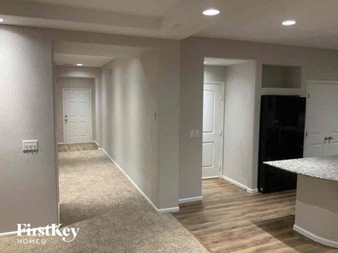 A spacious room with a carpeted floor and a kitchen area with a black fridge.