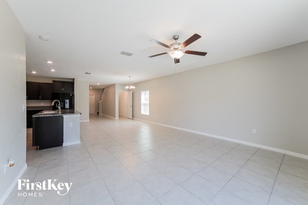 A spacious room with a ceiling fan and a kitchen area in the background.