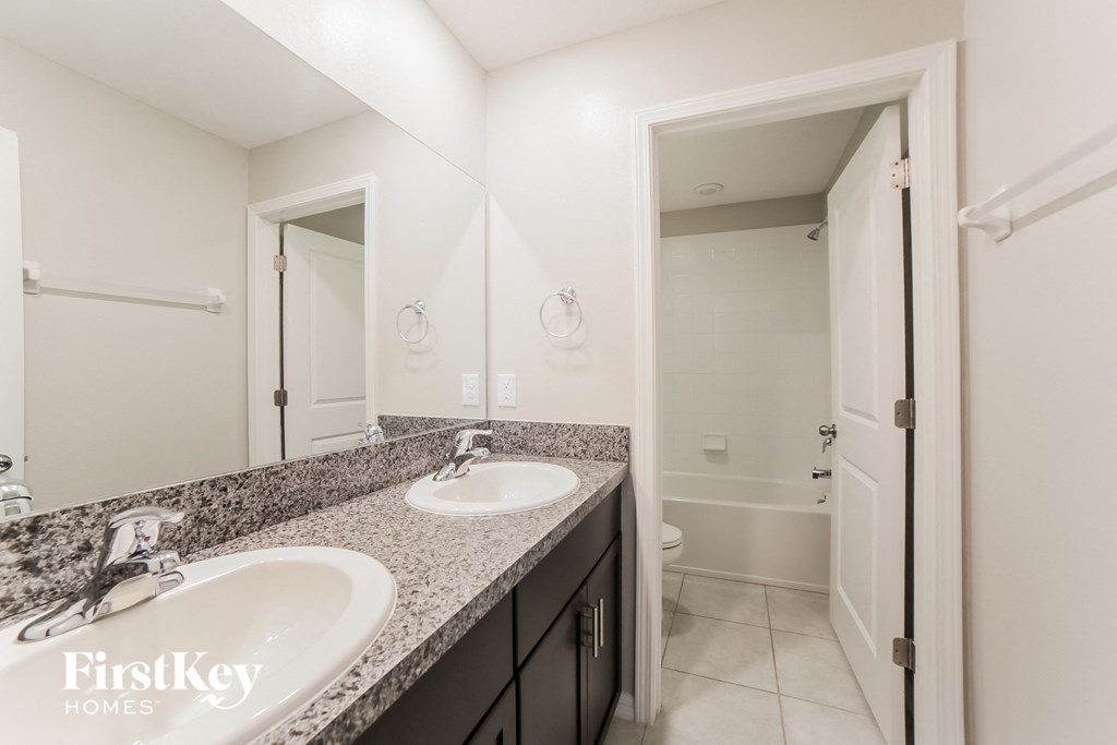 A bathroom with a double sink vanity and a toilet in the background.