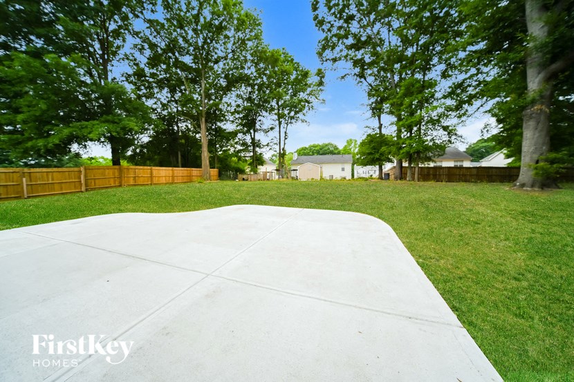 a large concrete area in a yard with trees and a fence