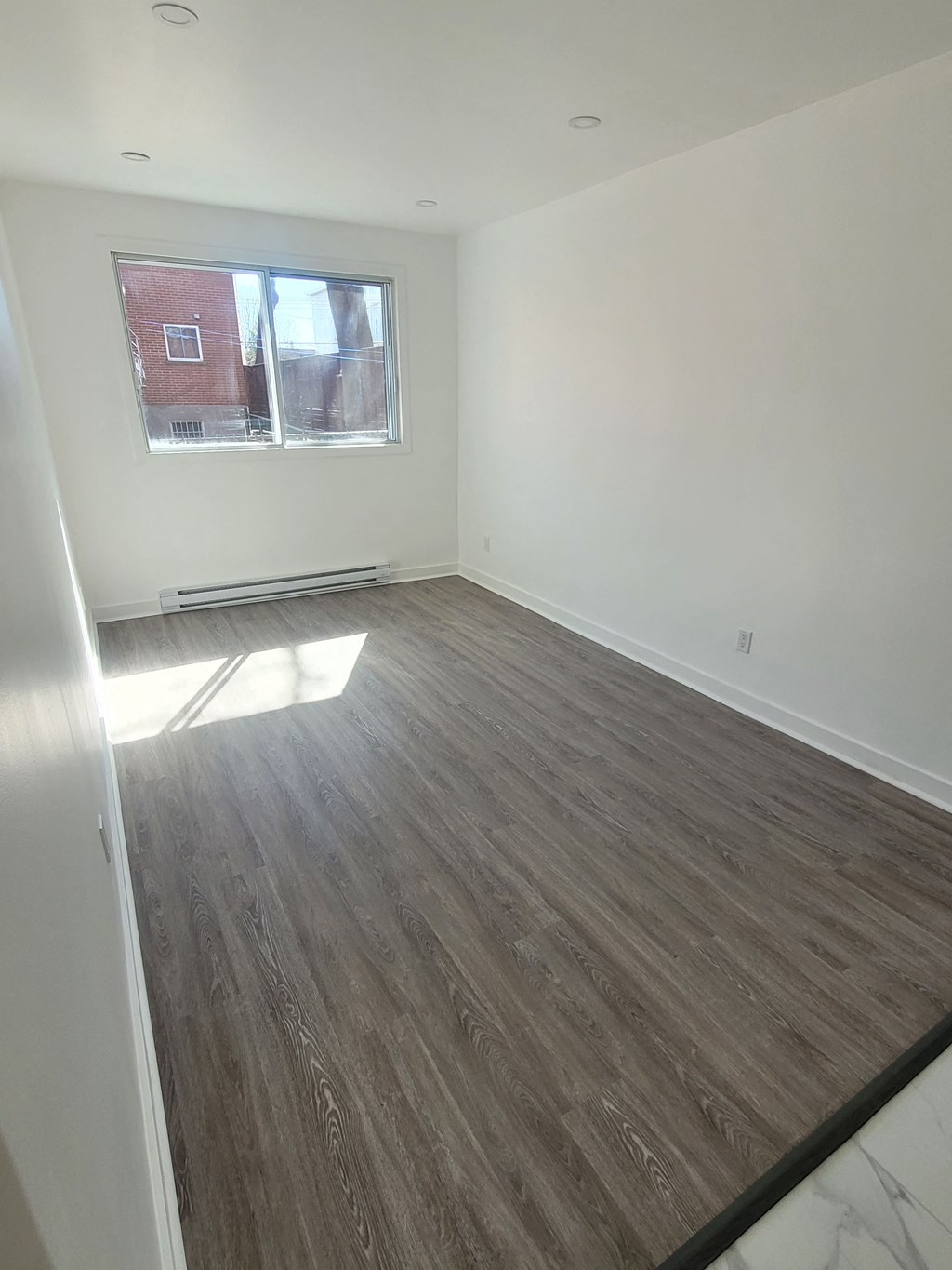 an empty living room with wood flooring and a window