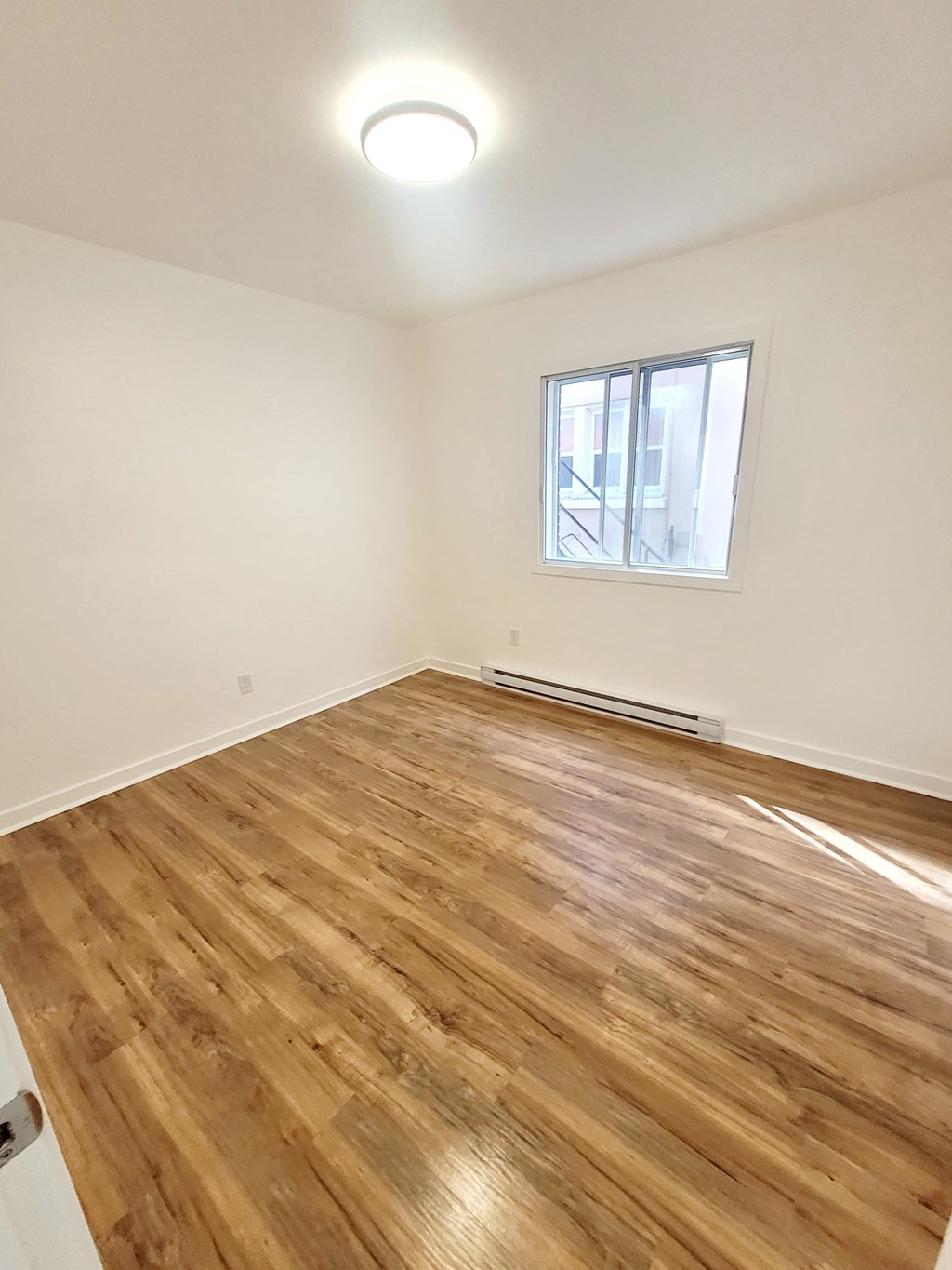 an empty living room with wood flooring and a window