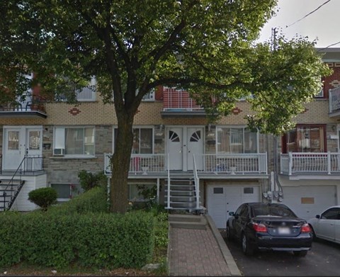 A tree in front of a two-story building with a car parked in front.