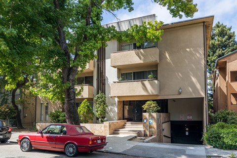 A red car is parked in front of a tan building.