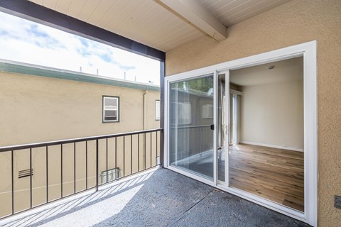 A balcony with a glass door leading to an empty room.