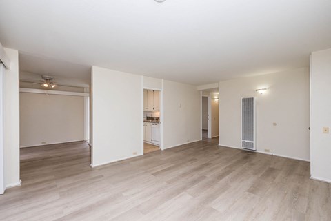 the living room and kitchen of an empty apartment with wood floors and white walls