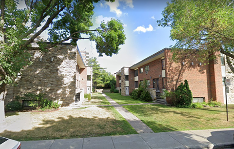 a sidewalk between two brick buildings with grass and trees