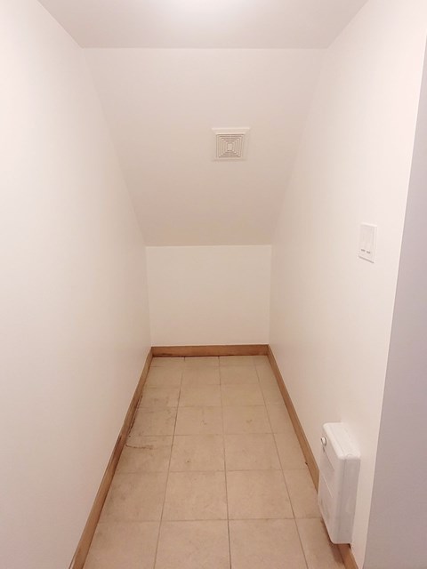 A white wall with a light switch and a white radiator on the floor.