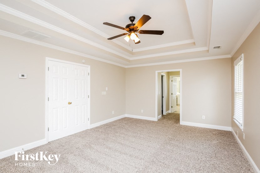 an empty living room with a ceiling fan and a door to a hallway