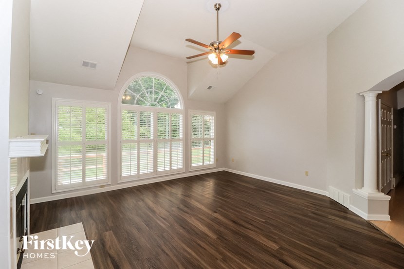 an empty living room with a ceiling fan and large windows
