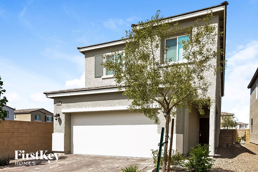 A modern house with a garage and a tree in front.